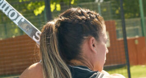 Woman with braided brown hair has back to the camera, holding a padel board.