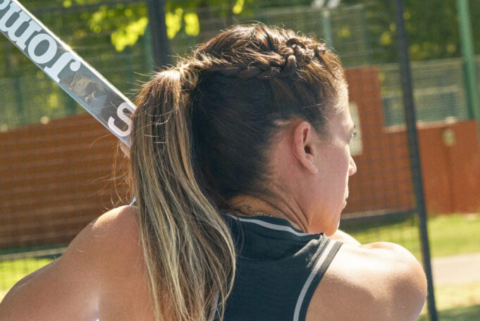 Woman with braided brown hair has back to the camera, holding a padel board.