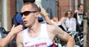 Male runner in GB vest has short cropped dark hair and wears dark sunglasses.