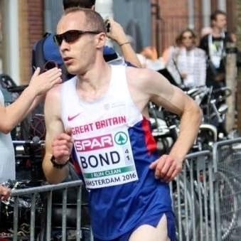 Male runner in GB vest has short cropped dark hair and wears dark sunglasses.