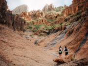 Three runners run away from the camera in a small rocky valley