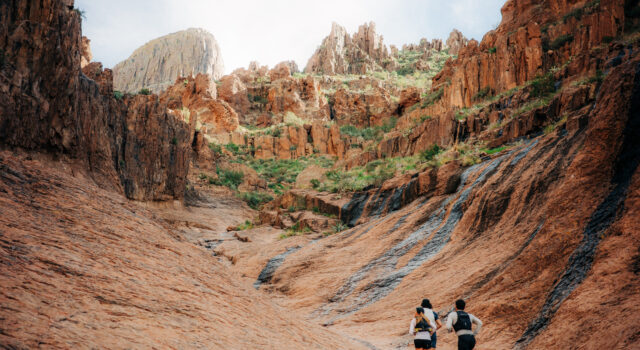 Three runners run away from the camera in a small rocky valley