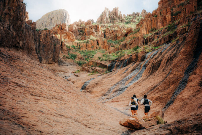 Three runners run away from the camera in a small rocky valley