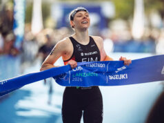A female triathlete smiles as she grabs the finishing tape to cross the line