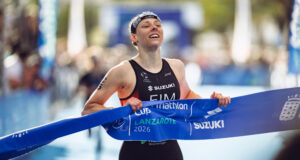 A female triathlete smiles as she grabs the finishing tape to cross the line