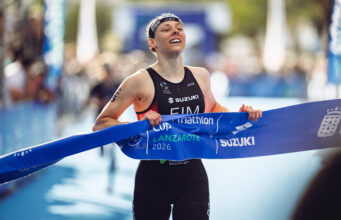 A female triathlete smiles as she grabs the finishing tape to cross the line