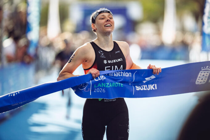 A female triathlete smiles as she grabs the finishing tape to cross the line