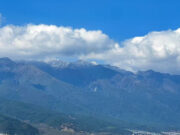 A bay of blue water with rocky mountains behind it. A city nestles between mountains and sea