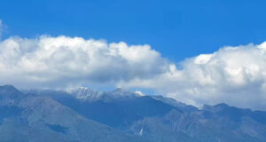 A bay of blue water with rocky mountains behind it. A city nestles between mountains and sea