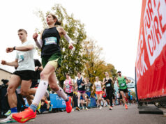 a male and female runner run past a camera on the ground. Behind them, many other runners are visible.
