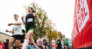 a male and female runner run past a camera on the ground. Behind them, many other runners are visible.