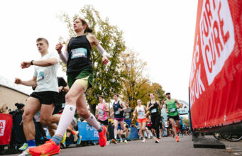 a male and female runner run past a camera on the ground. Behind them, many other runners are visible.