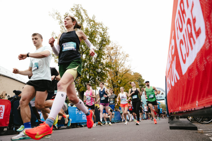 a male and female runner run past a camera on the ground. Behind them, many other runners are visible.