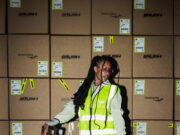 Saucony dispatches RUSH Woman stands on a pallet holding the handle of a pallet truck. She is wearing a hi vis jacket over sports kit and not looking directly at the camera.