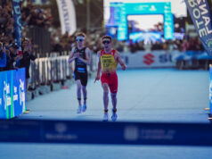 A male triathlete in yellow and red sprint to finish line just ahead of another athlete in black