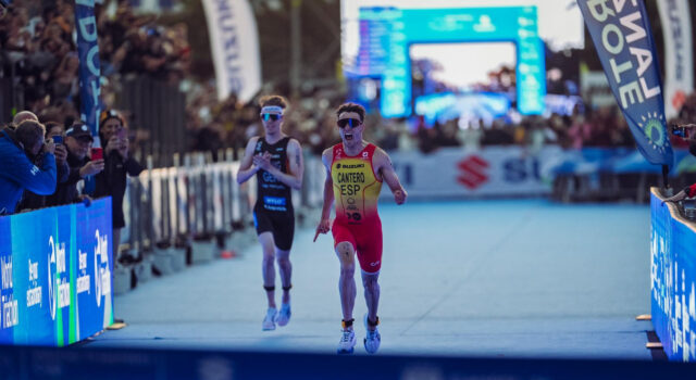 A male triathlete in yellow and red sprint to finish line just ahead of another athlete in black