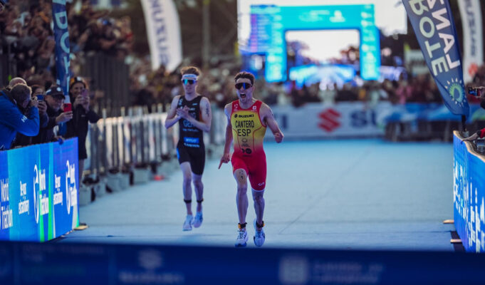 A male triathlete in yellow and red sprint to finish line just ahead of another athlete in black