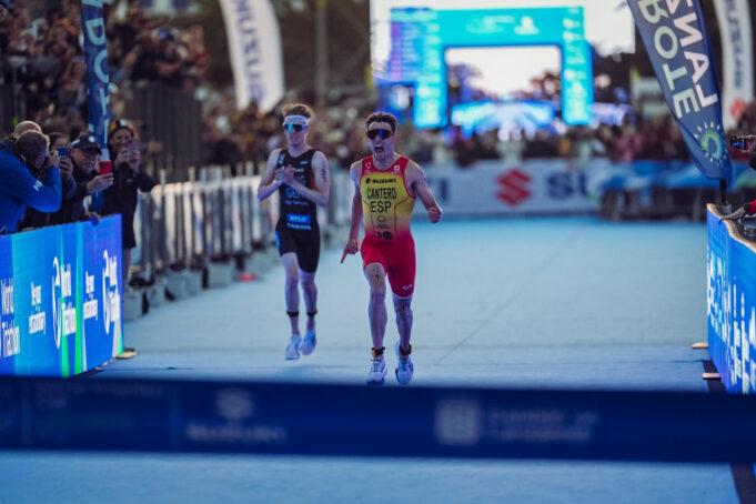 A male triathlete in yellow and red sprint to finish line just ahead of another athlete in black