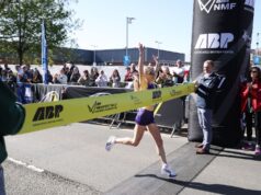 Woman crosses the line with arms above her head as she strides through the finishing tape