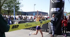 Woman crosses the line with arms above her head as she strides through the finishing tape