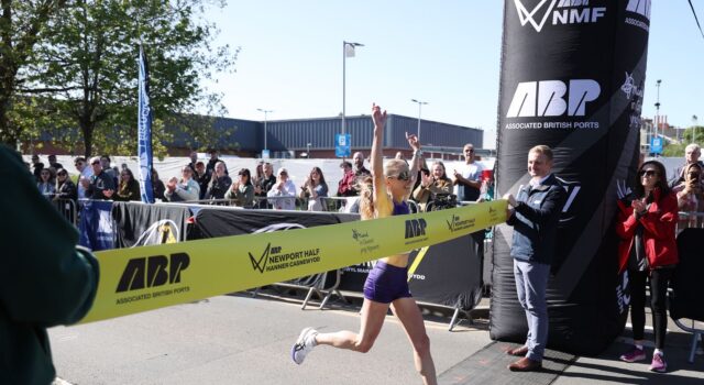 Woman crosses the line with arms above her head as she strides through the finishing tape