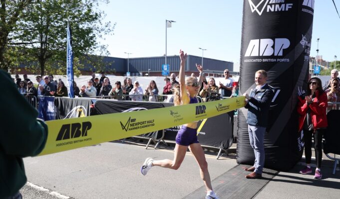 Woman crosses the line with arms above her head as she strides through the finishing tape