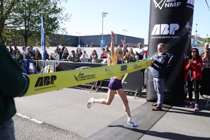 Woman crosses the line with arms above her head as she strides through the finishing tape