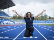 Woman kneels at the finish line with arms in the air