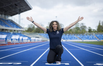 Woman kneels at the finish line with arms in the air