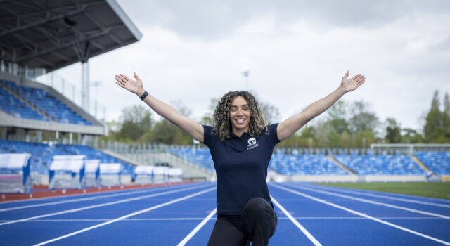 Woman kneels at the finish line with arms in the air