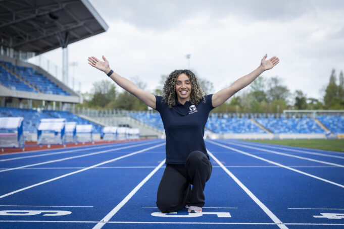 Woman kneels at the finish line with arms in the air