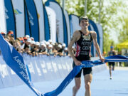Female triathlete has a smile on her face as she jogs through the finishing tape