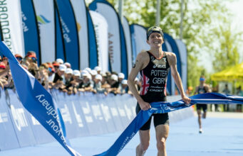 Female triathlete has a smile on her face as she jogs through the finishing tape
