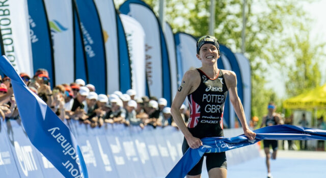 Female triathlete has a smile on her face as she jogs through the finishing tape