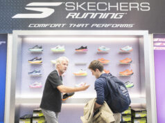 A man on a Skechers running stand shows another man some shoes