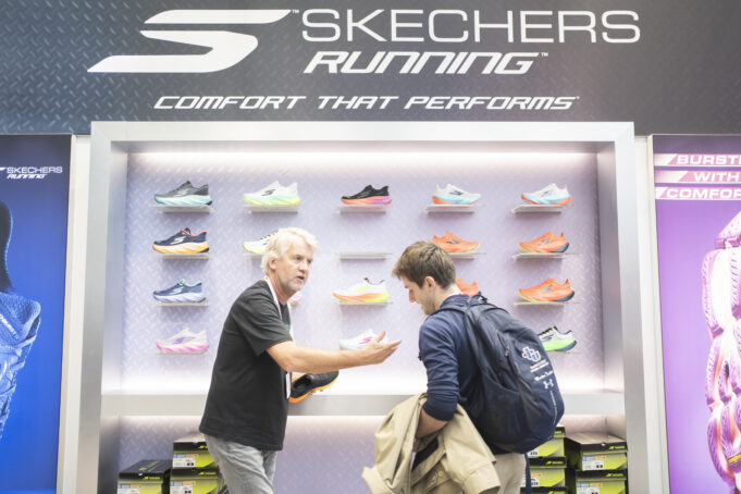 A man on a Skechers running stand shows another man some shoes