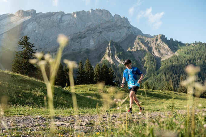 A lone male trail runner runs past craggy mountains in a green valley.