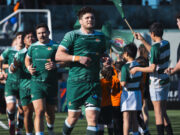 Male rugby players in green run out onto a pitch