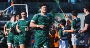 Male rugby players in green run out onto a pitch