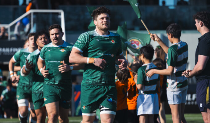 Male rugby players in green run out onto a pitch