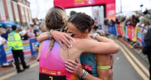 Two female runners hug beyond the finish gantry