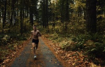 A topless male runner on a track through a forest