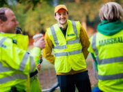 Ealing Half Marathon calls for volunteers Three marshals in hi-vis vests chat and smile. One male holds a takeaway coffee in his hand