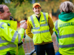 Three marshals in hi-vis vests chat and smile. One male holds a takeaway coffee in his hand