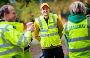 Ealing Half Marathon calls for volunteers Three marshals in hi-vis vests chat and smile. One male holds a takeaway coffee in his hand