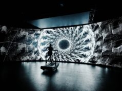 Psychedelic-inspired 24-Hour treadmill challenge A lone treadmill runner in front of a large screen showing a black and white kaleidoscopic image