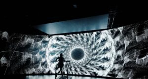 A lone treadmill runner in front of a large screen showing a black and white kaleidoscopic image