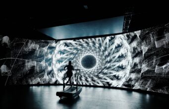 Psychedelic-inspired 24-Hour treadmill challenge A lone treadmill runner in front of a large screen showing a black and white kaleidoscopic image