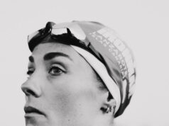 Black and whiite image of a head and shoulders shot of woman in a wetsuit with goggles and swimcap on head