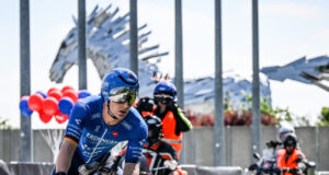 A triathlete on a bike with two support motorbikes behind hm